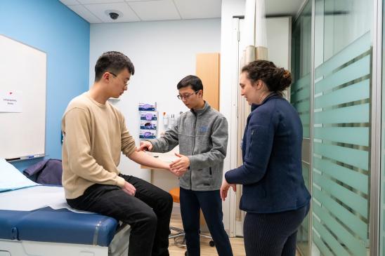 02/05/2025 - Boston, Mass. - Christopher Nguyen, M28, (center), practices testing a patient’s reflexes with his classmate Noah Feng, M28, with some assistance from Dr. Emma Lampropoulos, an intern at Tufts Medical Center, during a study session in the Simulation Center at the Tufts University School of Medicine on February 5, 2025. (Alonso Nichols/Tufts University)