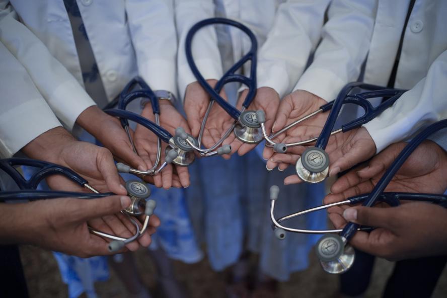 A circle of MD students holding stethoscopes in the palms of their hands