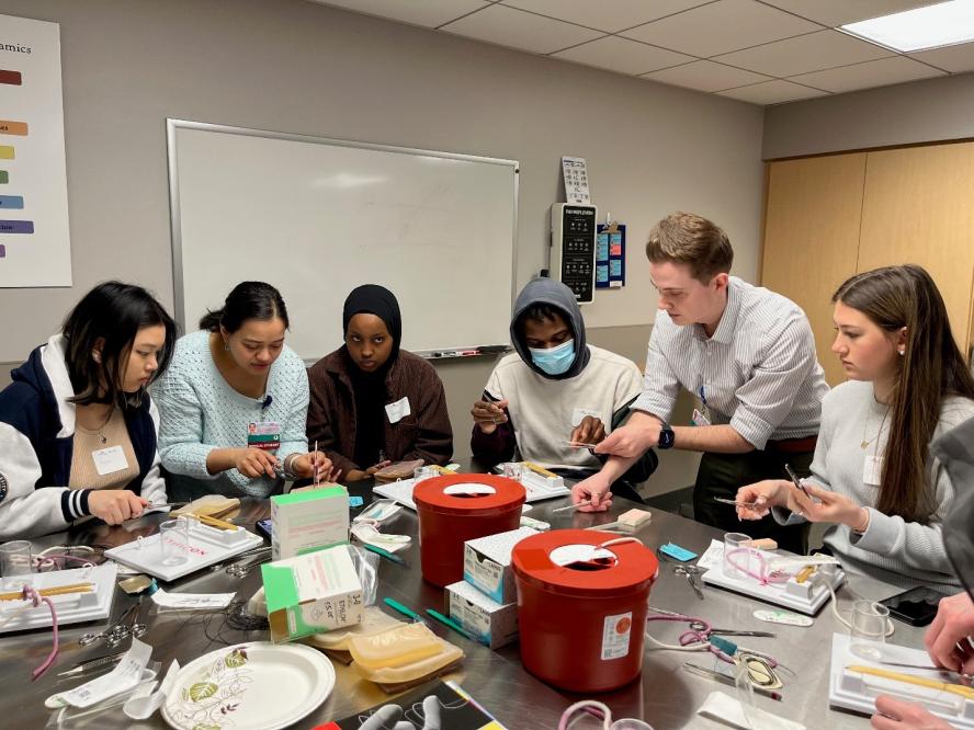 A group of high school students practicing suturing in a simulation center