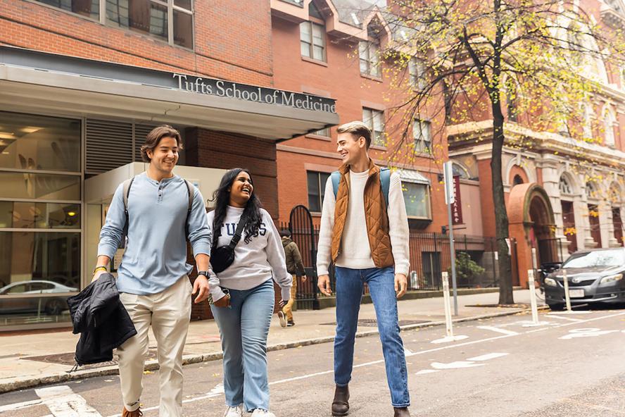 Three people walking, in front of Tufts School of Medicine building entrance