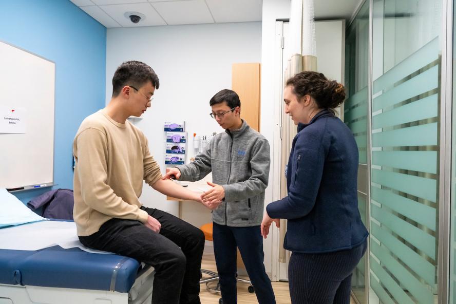 02/05/2025 - Boston, Mass. - Christopher Nguyen, M28, (center), practices testing a patient’s reflexes with his classmate Noah Feng, M28, with some assistance from Dr. Emma Lampropoulos, an intern at Tufts Medical Center, during a study session in the Simulation Center at the Tufts University School of Medicine on February 5, 2025. (Alonso Nichols/Tufts University)