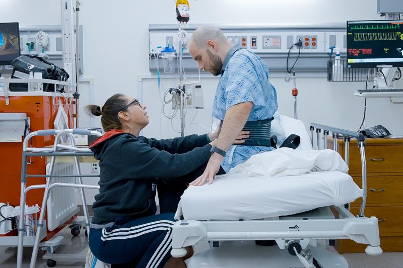 DPT student in clinical lab at hospital helping patient as patient gets up from bed