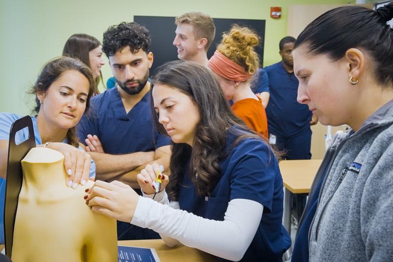 Tufts PA students watch faculty demo on high fidelity mannequin. 