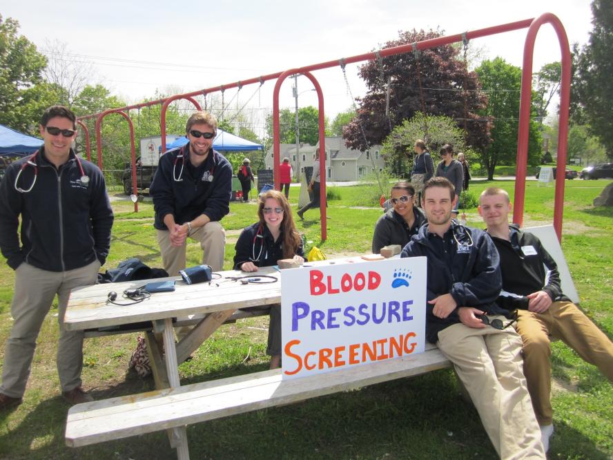 Medical student around a bench with a sign that says blood pressure screening