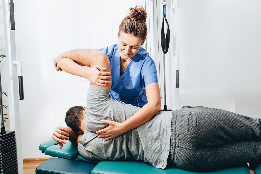 Physiotherapist holding patient's hand and shoulder joint during treatment