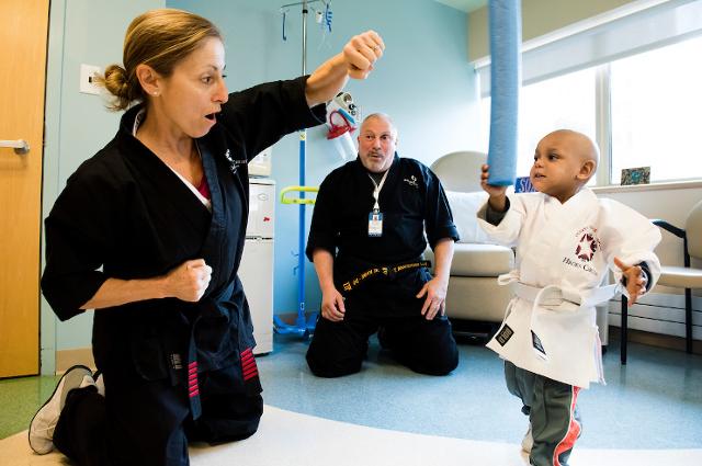 Two adults show a karate move to a young patient at a hospital