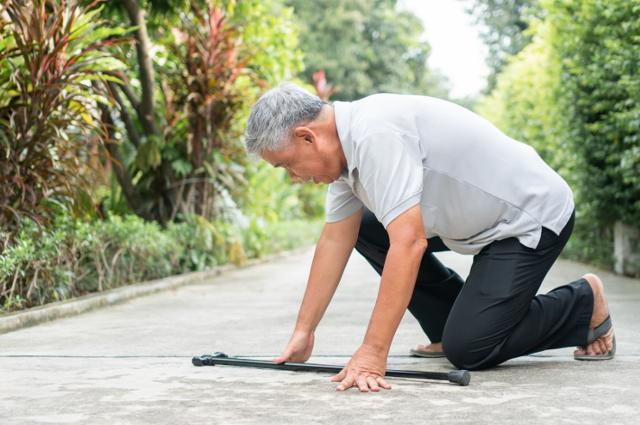 Elderly man picking up dropped cane from sidewalk