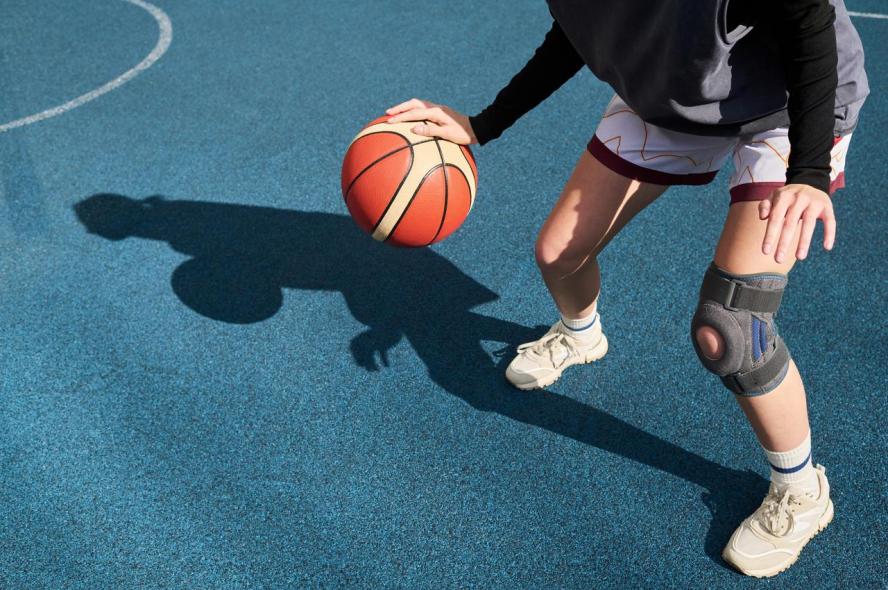 An overhead view of a young white woman playing basketball with a brace on her left knee.