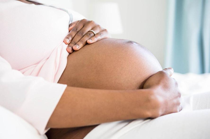 A pregnant Black woman with her hands on her belly 