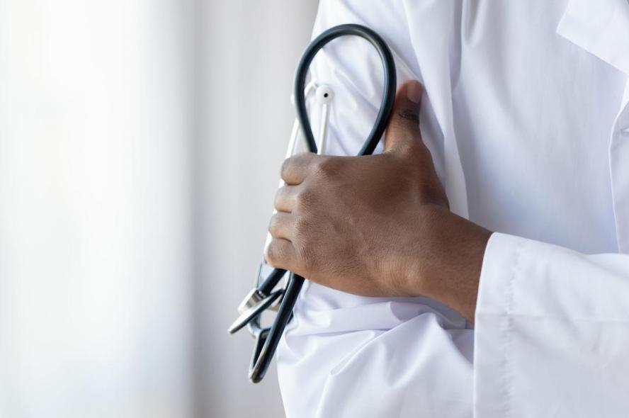 A Black doctor in a white lab coat holding a stethoscope.