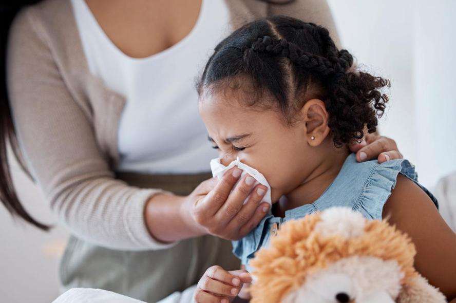 A mother helps a young child blow their nose with a tissue.