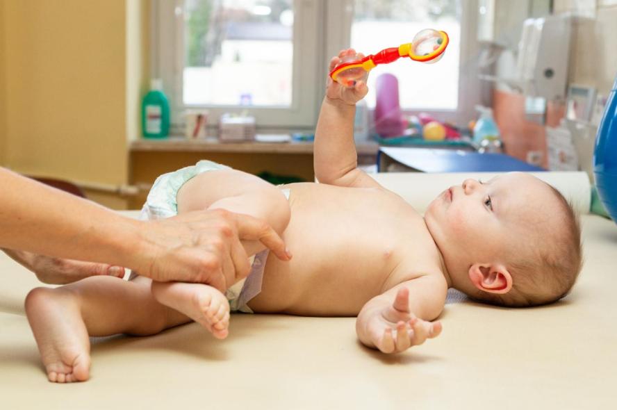 A baby in a diaper laying down with a physical therapist stretching the baby&#039;s leg