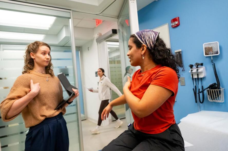 One woman stands and speaks to a woman on an exam table.