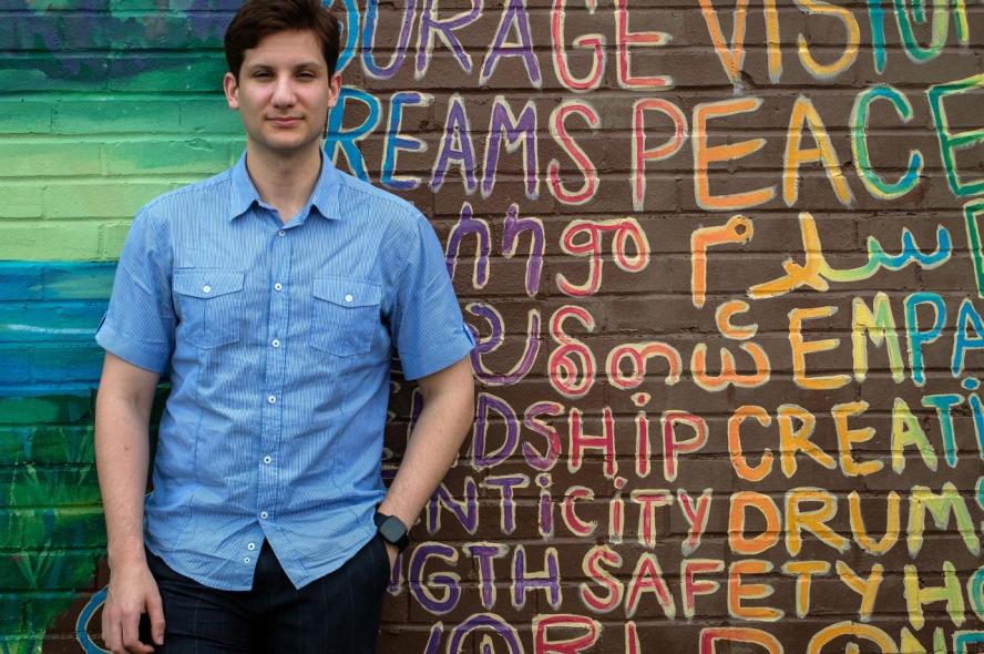 Abdallah Al-Obaidi, M25, is pictured in a light blue shirt against a colorful wall outdoors in Atlanta in June 2021 