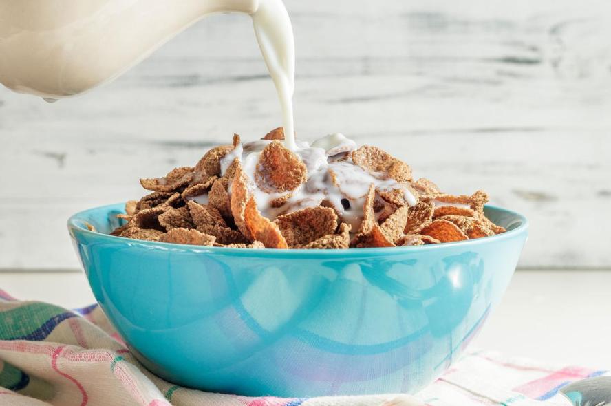 A bowl of fortified bran flakes cereal with milk being poured over it
