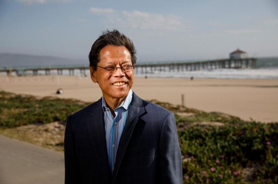 Dr. Sam W. Ho in a blue blazer and shirt, standing in front of a beach and pier