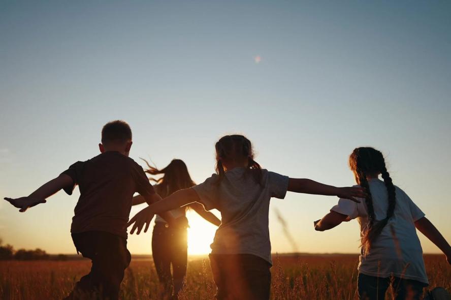 Four kids running through a field at sunset