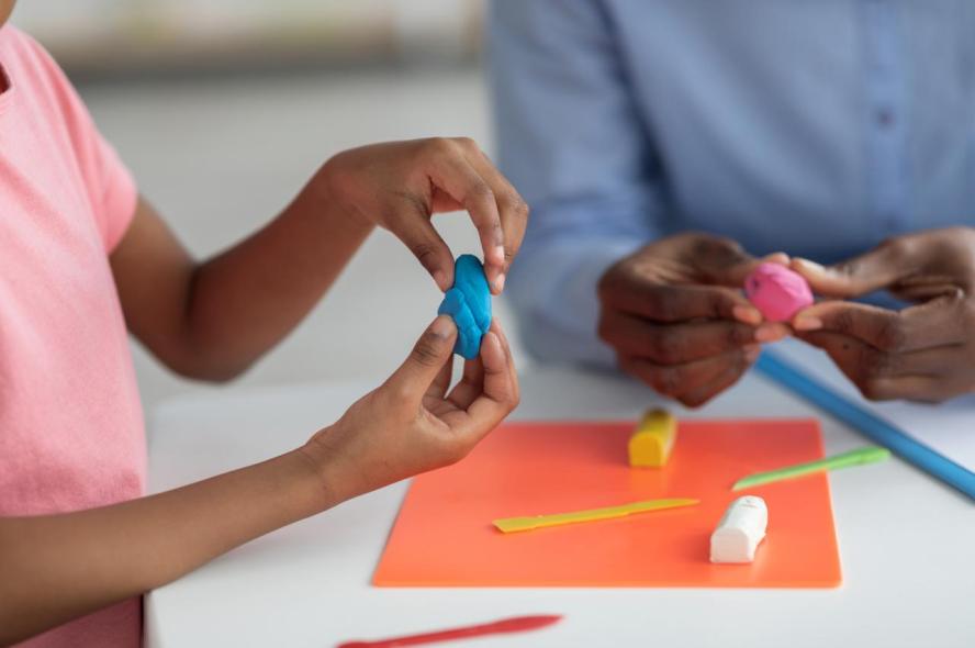 The hands of a young child and an adult using colorful clay at a table.