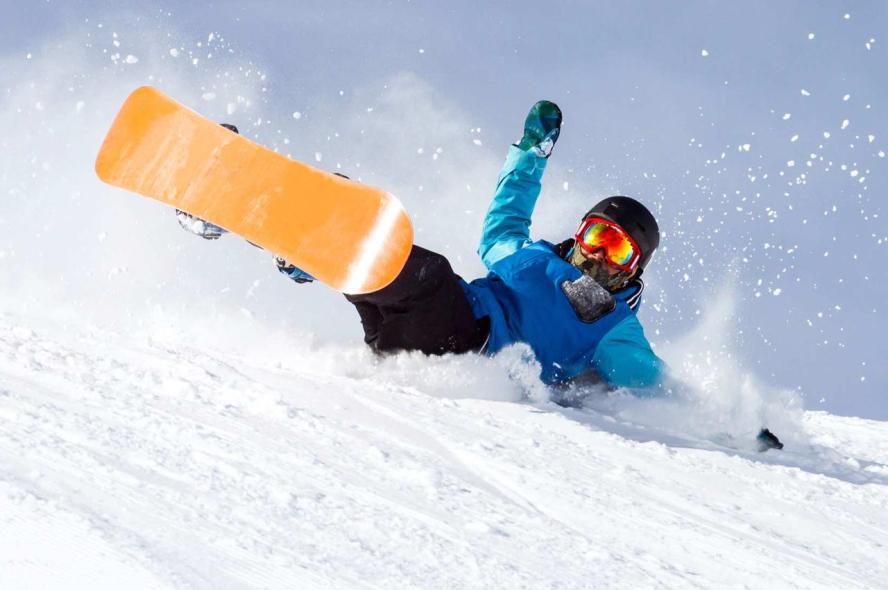 A snowboarder with a yellow board and blue coat falls on the snow