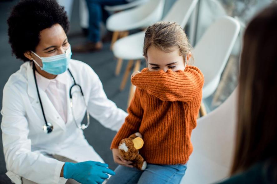 A medical professional checks on a coughing child in a waiting room.