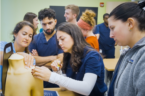Tufts PA students watch faculty demo on high fidelity mannequin. 