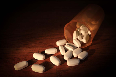 An open bottle spills white pills on a table. A Tufts assessment of 10 states identifies the communities most at risk for overdose deaths and most in needs of services.