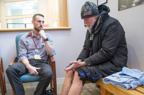 In this photo from 2017, physician Adam Normandin, MG11 (MBS), M15, listened to a homeless man at a Portland, Maine, clinic, as the patient soaked his feet in warm water and Epsom salt to treat frostbite.