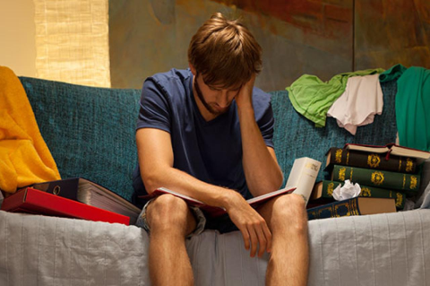 a male college student sitting on the couch looks tired