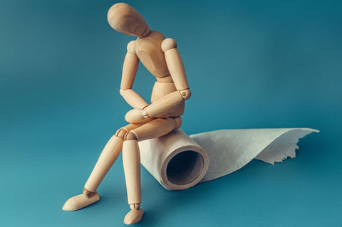 Wooden figure sit on a roll of toilet paper