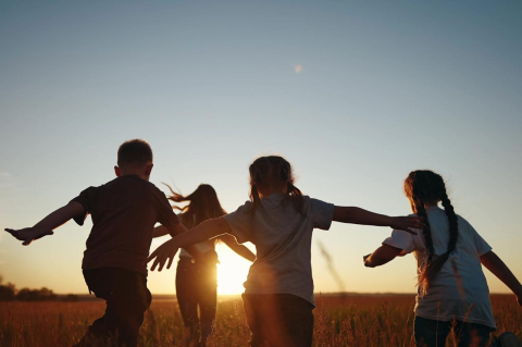 Four kids running through a field at sunset